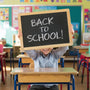 back to school sign being held by a boy at his desk