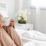 woman sitting on the bed sipping tea for self-care